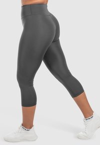 Leggings a vita alta di colore grigio scuro con una texture liscia, lunghezza cropped e cuciture piatte, abbinati a scarpe da ginnastica bianche.