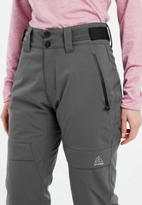 Gray ski pants feature a slim fit, with zippered side pockets, double button closure, and adjustable waistband. Logo visible on the thigh.