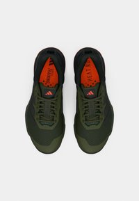 Chaussures de sport noires et vertes avec tige en maille, semelle texturée et accents orange. Présente un laçage visible et un logo sur la languette.