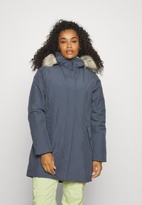 Námořnická parka s kapucí lemovanou umělým kožešinou, se zipovým zapínáním, postranními kapsami a délkou po kolena. Materiál má hladkou strukturu.
