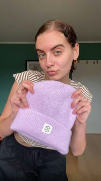 Berretto lavorato a maglia lilla con texture a coste e risvolto, caratterizzato da una piccola etichetta bianca con un logo impresso.