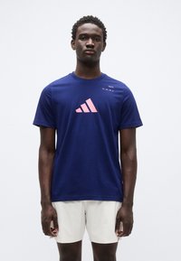 Μπλε ναυτικό αθλητικό t-shirt από βαμβάκι, με ροζ λογότυπο adidas, κοντά μανίκια, στρογγυλή λαιμόκοψη και την επιγραφή "PADDEL" στον ώμο.