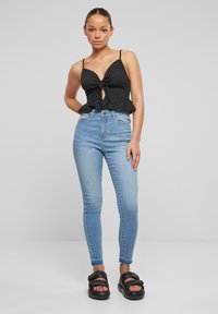 Černý žebrovaný peplum top s detailním uzlem vpředu, kombinovaný se světle modrými skinny džíny a černými platformovými sandály. Hladká textura a volný střih.