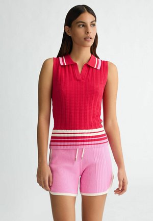 Top senza maniche a coste rosso con colletto a righe, abbinato a pantaloni corti a coste rosa chiaro con bordo bianco e cordoncino.