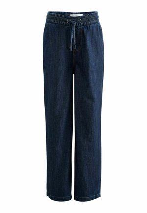 Nærbillede af en person iført mørke denim bukser med elastisk talje og bundet snøre samt en hvid ribstrikket top, der er stukket ind.