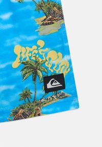 Μπλε τροπικό πουκάμισο με σχέδιο παλμών και νησιών, με την ένδειξη "LIFE'S A QUAD" σε κίτρινο χρώμα. Περιλαμβάνει ένα μαύρο λογότυπο. Απαλή ύφανση.