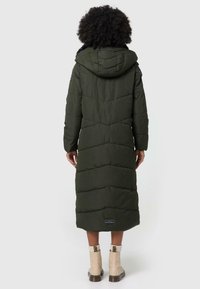 Long, olive green puffer coat with a hood, featuring quilted patterns and a logo on the bottom hem. Worn over beige ankle boots.