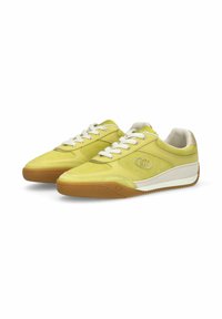 Paire de baskets en daim jaune et cuir avec lacets blancs, semelles en caoutchouc marron, et un logo argenté sur les côtés, orientées vers la droite.