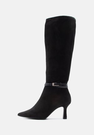 Botte noire en daim montant jusqu'au genou avec un bout pointu, un talon stiletto de hauteur moyenne et une fine bride décorative avec une petite boucle autour de la cheville.