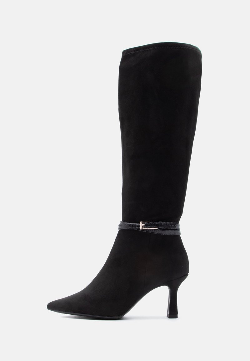 Botte noire en daim montant jusqu'au genou avec un bout pointu, un talon stiletto de hauteur moyenne et une fine bride décorative avec une petite boucle autour de la cheville.