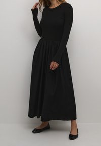 Czarna sukienka z długim rękawem, z prążkowanym górnym częścią i zgromadzoną, zwiewną spódnicą. Gładka tekstura, sięgająca do połowy łydki, zestawiona z czarnymi balerinami.