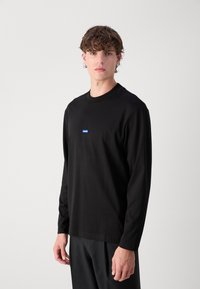 Zwarte lange mouw T-shirt van katoen, met een klein blauw rechthoekig logo op de borst, ronde halslijn en een relaxte pasvorm.