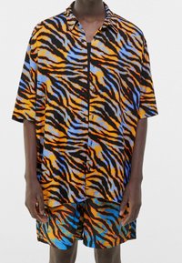 Zestaw składający się z koszuli z krótkim rękawem i spodenek z żywym wzorem tygrysich pasków w kolorach pomarańczowym, niebieskim i czarnym; wykonany z lekkiego materiału.