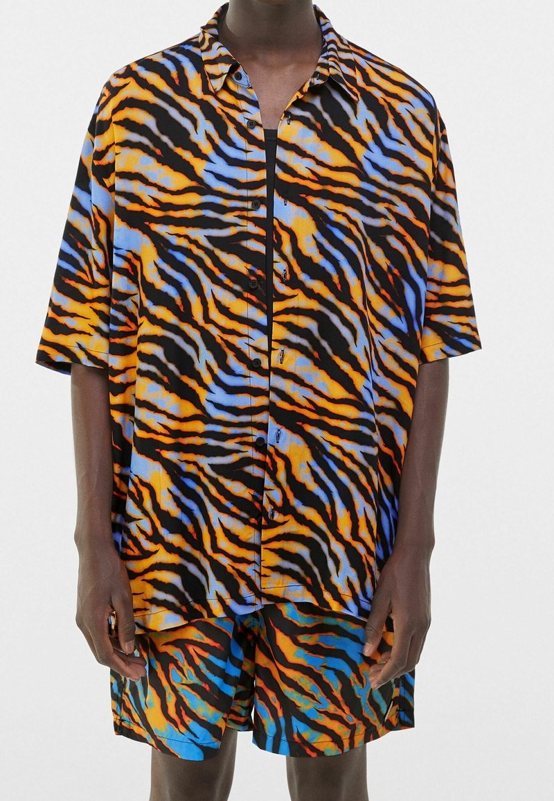 Zestaw składający się z koszuli z krótkim rękawem i spodenek z żywym wzorem tygrysich pasków w kolorach pomarańczowym, niebieskim i czarnym; wykonany z lekkiego materiału.