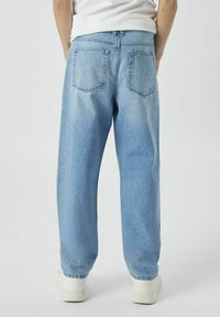 Jeans de mezclilla azul claro con un corte relajado, dos bolsillos traseros y una cintura alta, combinados con zapatillas blancas.