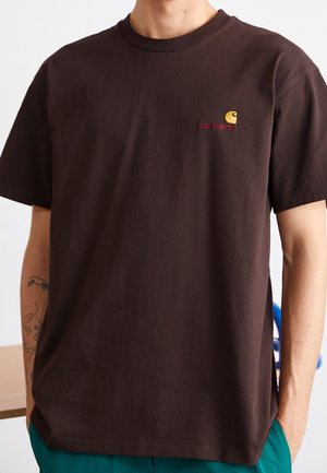 Braunes Baumwoll-T-Shirt mit einem gerippten Rundhalsausschnitt und einem kleinen, gelb-roten gestickten Logo auf der linken Brustseite.