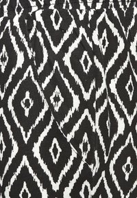 Schwarz-weißer Stoff mit einem Diamantenmotiv, der eine strukturierte Oberfläche und einen leichten Glanz aufweist. Enthält ein sichtbares Taschen-Detail.
