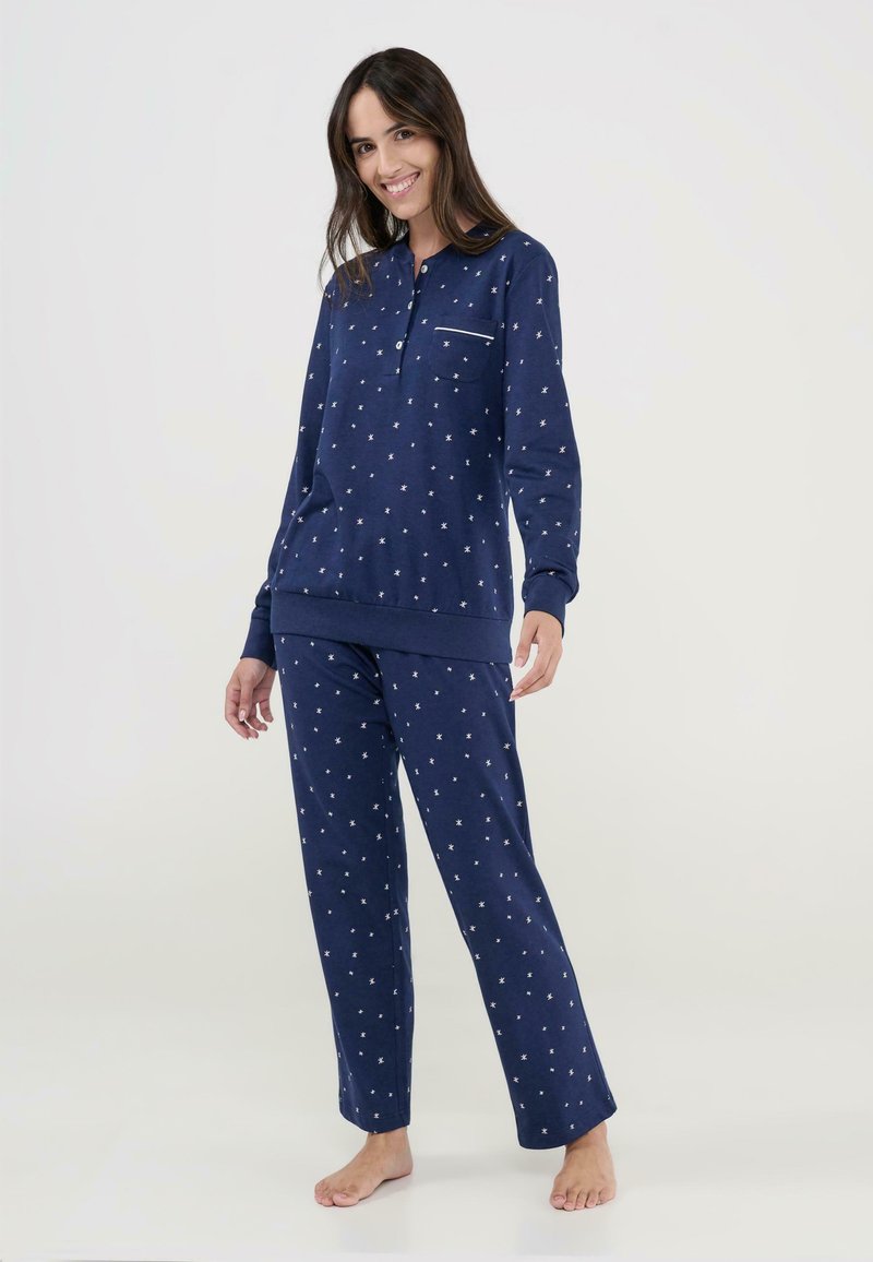 Conjunto de pijama azul marino hecho de tela suave, que incluye una camiseta de manga larga con un bolsillo y patrones de estrellas blancas, acompañado de pantalones a juego.