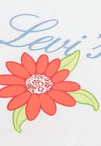 Λευκό ύφασμα με σχέδιο κόκκινου λουλουδιού και πράσινα φύλλα. Το "Levi's" είναι τυπωμένο με γαλάζια καλλιγραφικά πάνω από το λουλούδι.