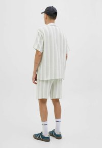 Camisa de manga corta a rayas verde claro y pantalones cortos a juego, de tela de mezcla de algodón, corte relajado, combinados con zapatillas azules y calcetines blancos.
