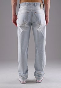 Helle blaue Denim-Jeans mit einer lockeren Passform, ausgestattet mit Gesäßtaschen mit Kupfernieten und einem braunen Lederetikett am Bund.