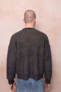 Tumšs vilnas maisījuma džemperis ar vertikālām svītrām olīvzaļā un melnā krāsā, mērenas platuma piegriezums un riboti aproces un apakšmala.