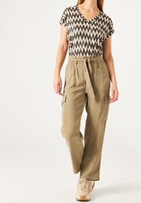 Beige cargo pants with side pockets and a drawstring waistband, paired with a short-sleeved, black and cream zigzag patterned top.