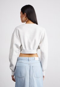 Kuttet grå sweatshirt med senkende skuldre, ribbestrikket kant og myk tekstur, sammen med et lys blått denimskjørt med baklommer.