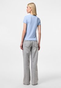 Haut côtelé bleu clair à manches courtes et bords festonnés, associé à un jean gris clair à jambes larges avec poches arrière.