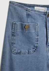 Jeans en denim bleu clair avec une poche avant et une fermeture à bouton en métal, une texture subtile et des détails cousus. Étiquette de marque visible à l'intérieur.