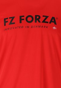 Punainen t-paita, jossa mustalla printatulla tekstillä "FZ FORZA" ja "INNOVATED IN DENMARK", pieni Tanskan lipun yksityiskohta. Pehmeä kangas.