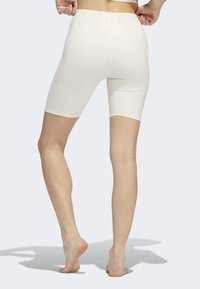 Bílé vysoké šortky s hladkým povrchem, tvarované do poloviny stehna, s kontrastními švy a dvěma zadními kapsami.