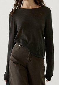 Svart långärmad skjorta i lätt material med avslappnad passform, med rund halsringning och en böjd nederkant, kombinerad med bruna högmidjade byxor.