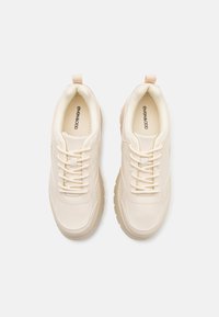 Baskets couleur crème avec une tige en synthétique lisse, des accents texturés et un design à lacets. Bout rond et semelle épaisse et rembourrée.