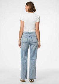 Svijetloplave traperice s visokim strukom i opuštenim krojem, s dvije stražnje džepove i poderanim rubovima, u kombinaciji s običnom bijelom majicom.