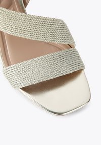 Sandales à brides en tissu tissé doré clair avec un design à bout carré, présentant un éclat métallique sur la semelle intérieure et des détails texturés.