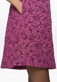 Rochie violet cu un model floral texturat. Designul are petale ridicate și este asortată cu ciorapi închiși la culoare. Potrivită pentru diverse ocazii.