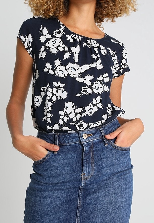 Femme portant un chemisier bleu marine à fleurs rentré dans une jupe en jean bleu taille haute, les mains dans les poches.