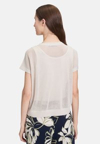 Jasno beżowa siatkowa bluzka z krótkim rękawem, okrągłym dekoltem i prążkowanym dołem. Posiada luźny krój, ukazując otwartą strukturę dzianiny.