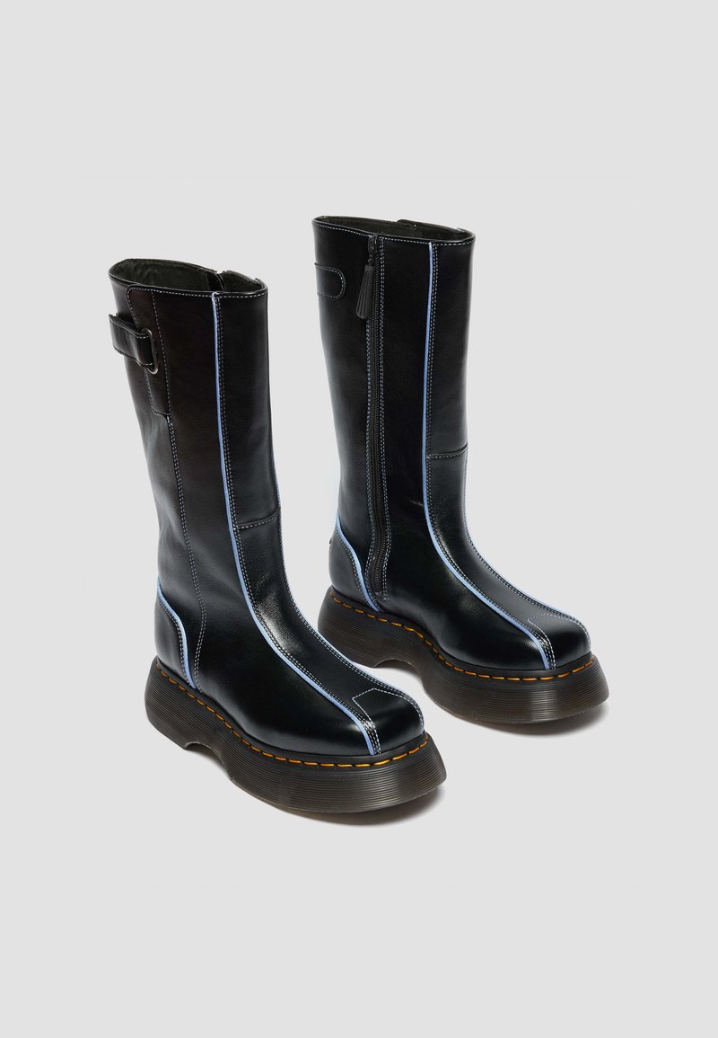 Tall black leather boots with thick brown soles, blue stitching along front and sides, and side zipper on a light gray background.