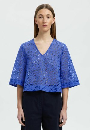 Blå, cropped bluse med V-hals og brede ærmer. Lavet af tekstureret stof med cirkulære udskæringer i hele designet, hvilket skaber en åndbar konstruktion.