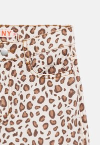 Παντελόνι με τύπωμα λεοπάρ, μπροστινή τσέπη και ασημένιο κουμπί, με μπεζ ύφασμα με ακανόνιστες καφέ βούλες και ορατά ραφές.