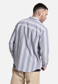 Camisa a rayas en azul y blanco, con un corte relajado, mangas largas y cuello abotonado. La tela tiene una textura ligera.