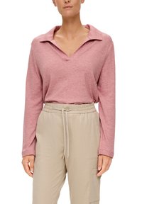 Pyjama w odcieniu przykurzonego różu z długim rękawem i szerokim kołnierzem, w luźnym kroju, zestawiona z jasnobeżowymi spodniami z elastycznym paskiem w pasie, posiadającymi kieszenie z przodu.