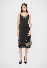 Black slip dress with lace accents, adorned with silver studs. Features adjustable straps and a scalloped hem. Paired with a small gray handbag.