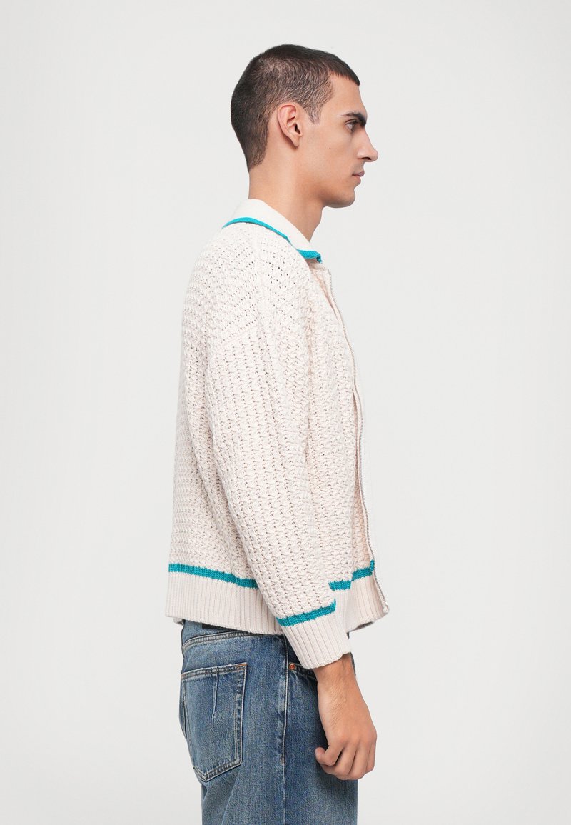 Light beige knitted cardigan with teal accents at the collar and hem. Features a textured pattern and ribbed cuffs. Slim fit design.