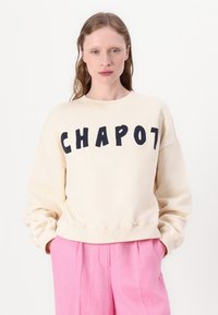 Krémová mikina s nápisom "CHAPOT" v tučných námorníckych písmenách, s okrúhlym výstrihom a mierne puffovými rukávmi.