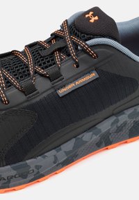 Czarne sportowe buty z siateczkowymi i tekstylnymi wykończeniami, pomarańczowymi akcentami oraz szarym, w kamuflażowym wzorze podeszwą. Zawierają sznurowadła oraz metkę z logo.
