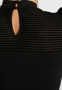 Schwarzes Oberteil mit gestreiftem, transparentem Oberteil, keyhole-Rücken mit zwei Knopfakzenten und einem glatten, eng anliegenden unteren Bereich.