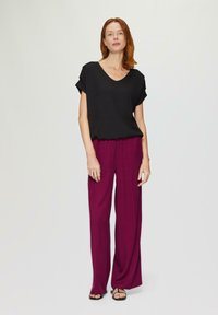 Zwarte V-hals top met korte opgerolde mouwen, gecombineerd met losse, vloerlange magenta broeken van lichtgewicht stof. Eenvoudige sandalen maken de look compleet.